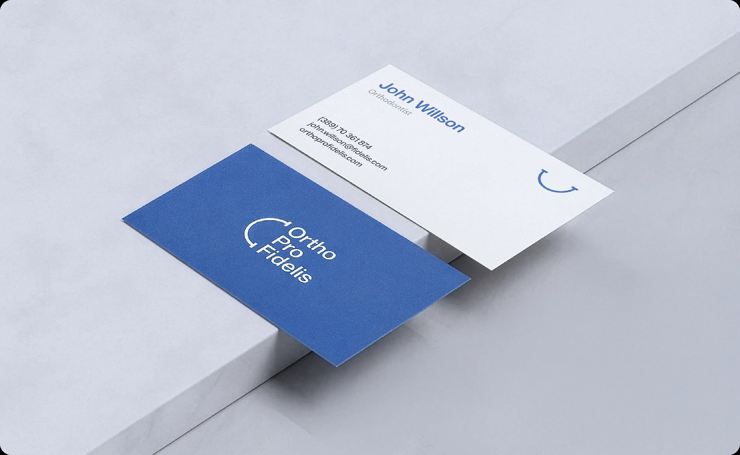 Ortho Pro Fidelis business cards on a pale plinth, logo side and contact side